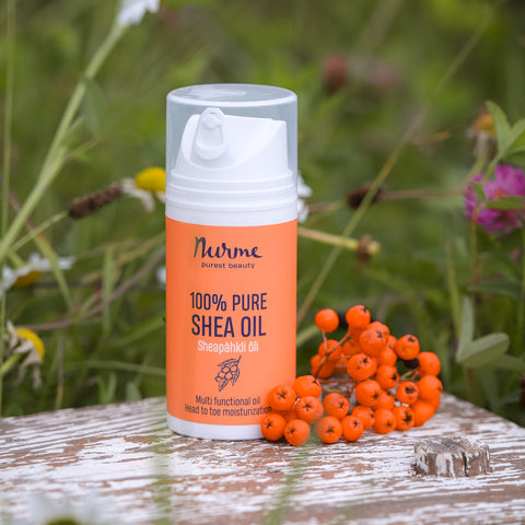 Nurme 100% Pure Shea Oil bottle on a rustic wooden surface with bright orange berries and greenery in the background, promoting natural skincare.