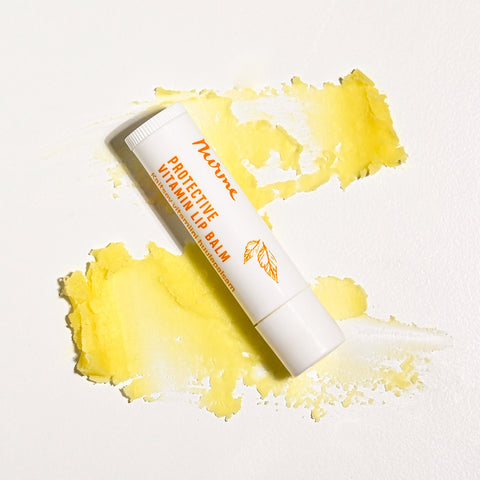 Nurme Protective Vitamin Lip Balm placed on a textured smear of yellow balm on a white background.