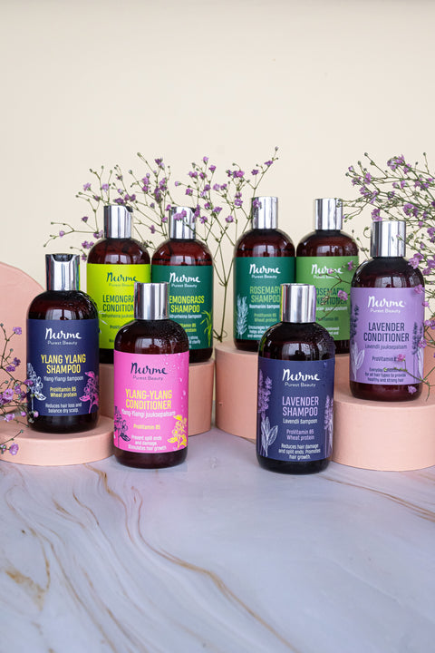 Two bottles of Nurme Lemongrass Shampoo, one small and one large, displayed on natural stone arrangements with fresh green leaves in the background.