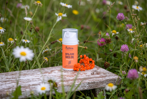 Nurme natural Pure Shea Oil on a wooden stool beside orange berries and meadow flowers