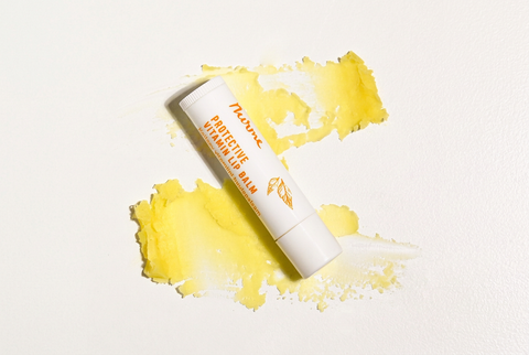 Nurme Protective Vitamin Lip Balm placed on a textured smear of yellow balm on a white background.